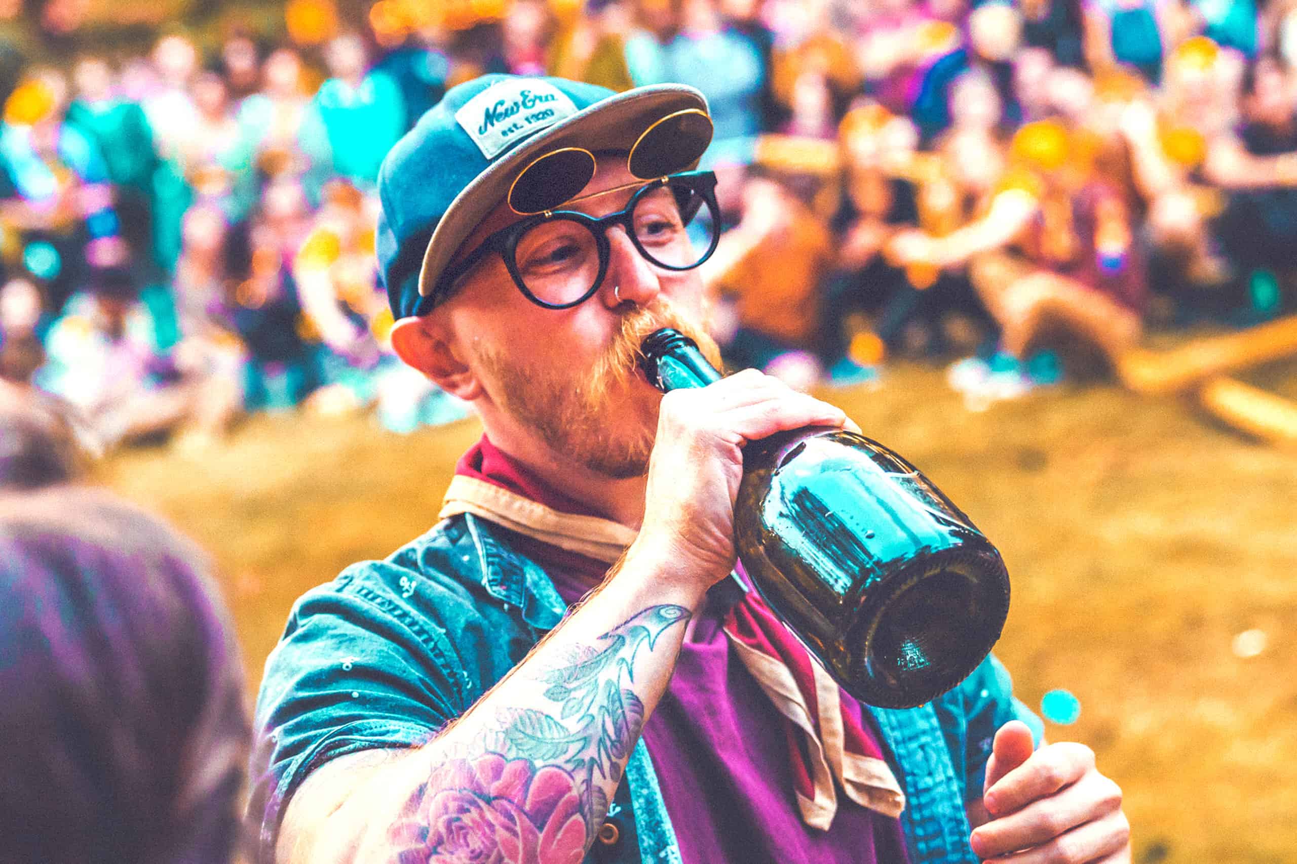 Man drinking from bottle with patrol scarf on at the patrol games at Camp Wildfire. A summer weekend break in a forest near London and Kent. An outdoor woodland retreat featuring adventure activities, live music, DJs, parties and camping. Half summer adventure activity camp, half music festival, for adults only.